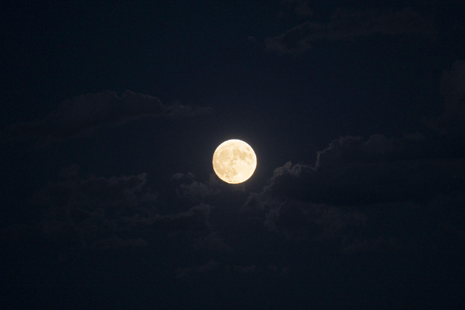 The full moon lights clouds in midnight blue sky